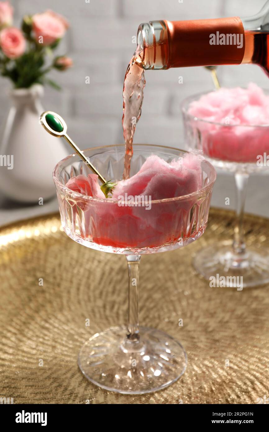 Pouring rose wine from bottle into glass with cotton candy on golden ...