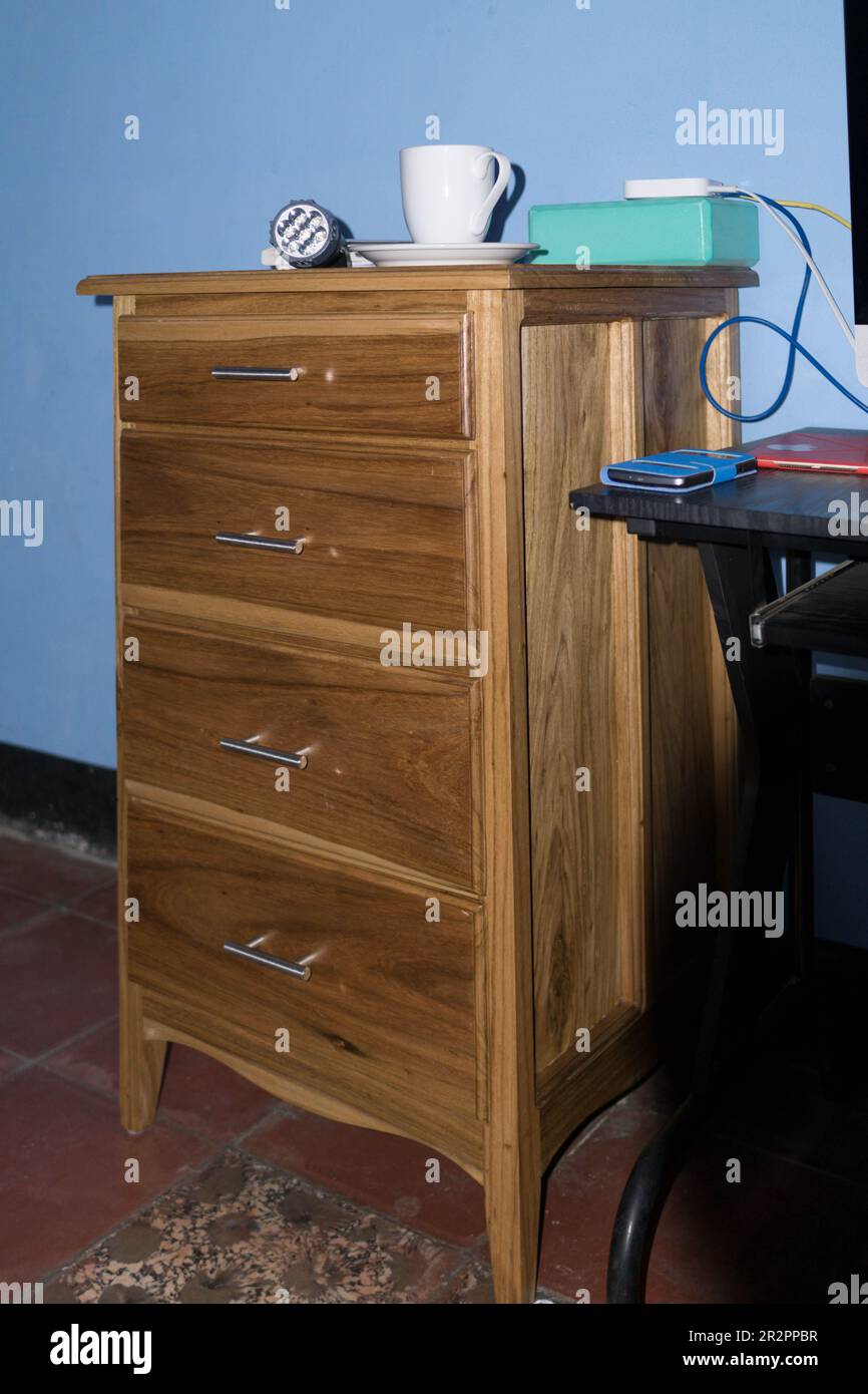 Small custom made chest of drawers in an office setting with coffee cup, flashlight, and internet router. Stock Photo