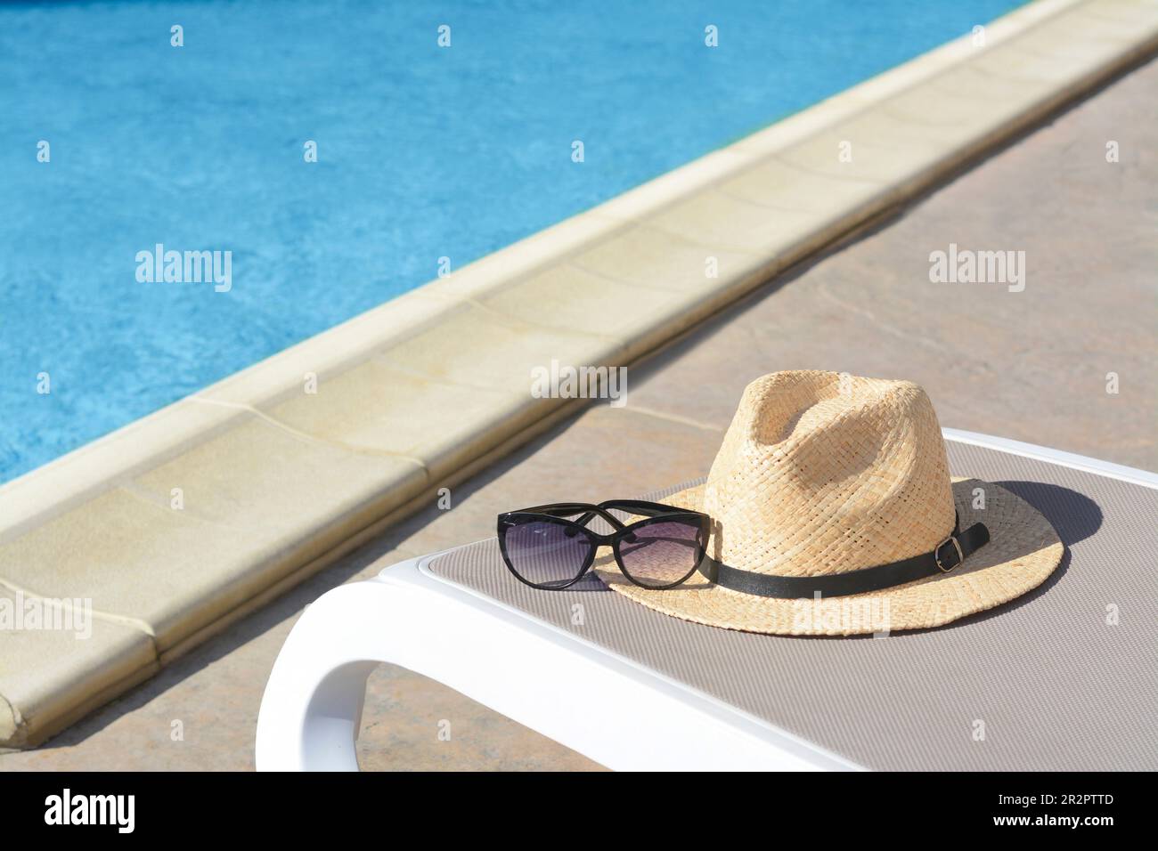 Stylish straw hat and sunglasses on grey sunbed at poolside. Beach ...