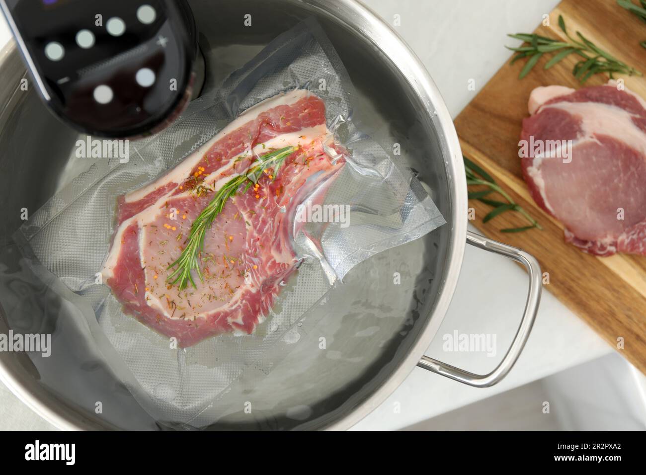 Sous vide cooker and vacuum packed meat in pot on white table, top view