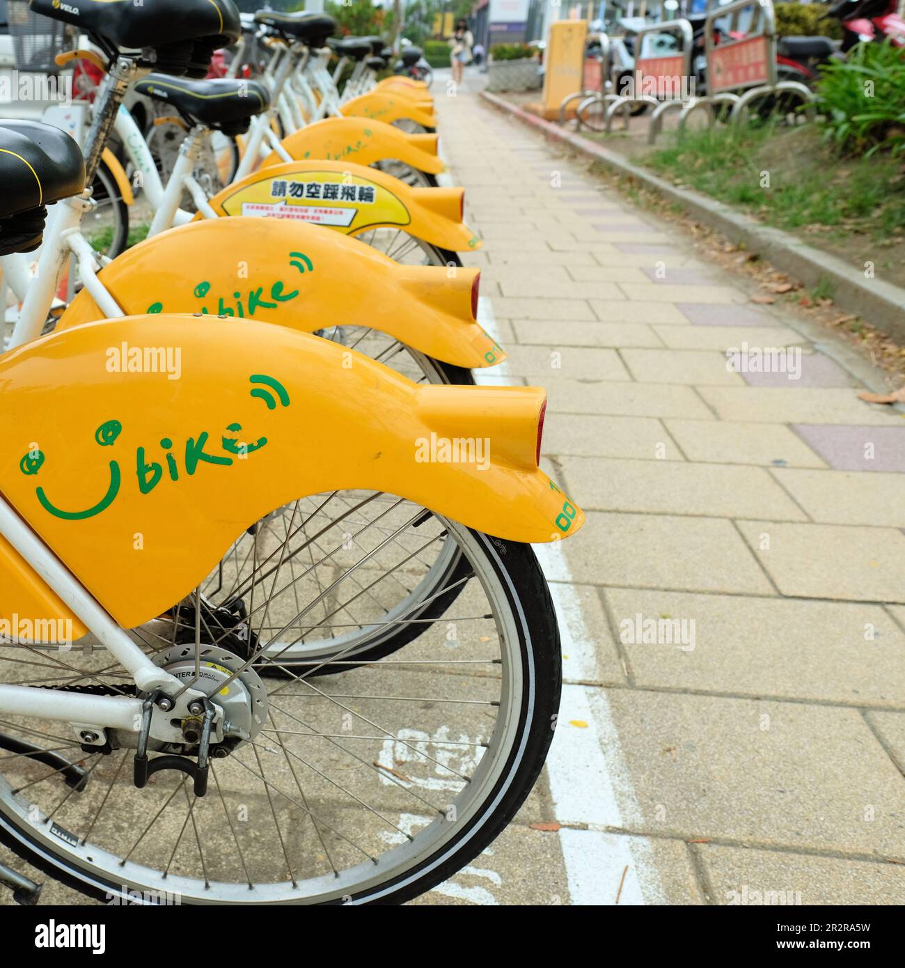 YouBike Smile Bikes along a sidewalk path in Kaohsiung City in southern Taiwan; yellow smile bicycles for rent for local commuters and tourists. Stock Photo