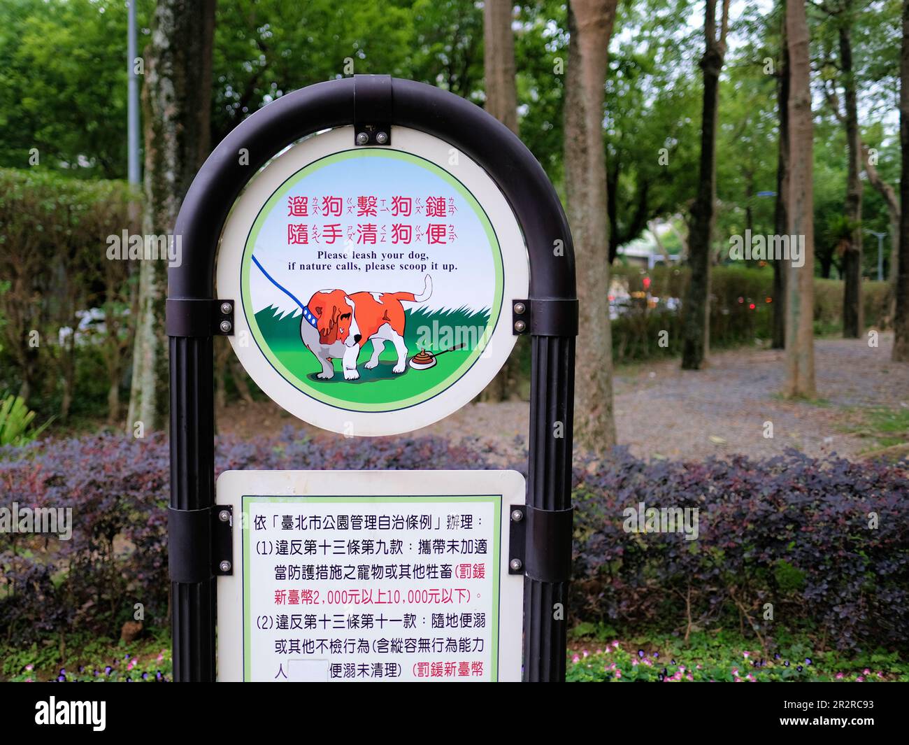 Bilingual sign in English and Chinese asking owners to leash and clean up after their dog; Daan Park Taipei, Taiwan; scoop it up, keep it leashed. Stock Photo