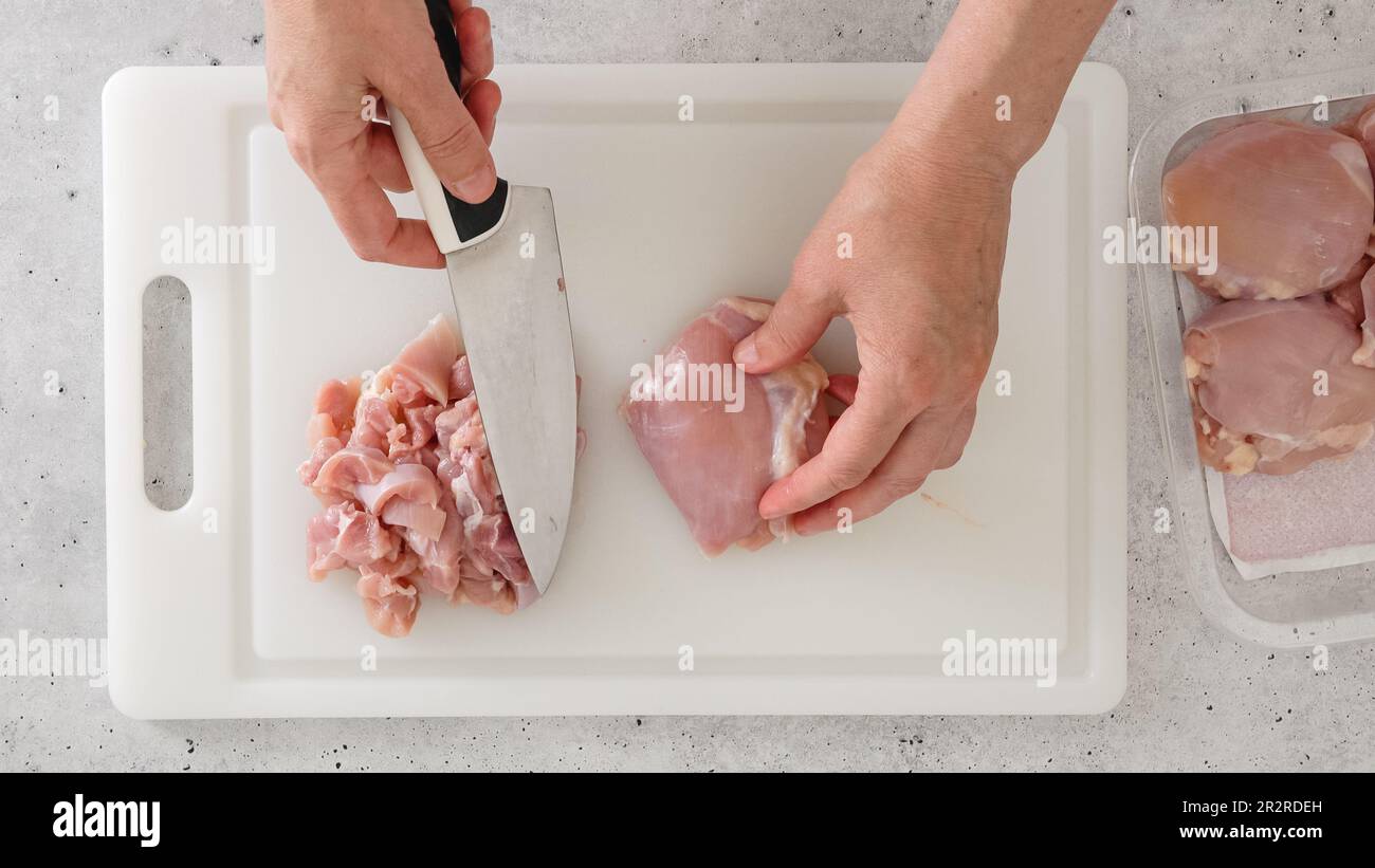 The woman cuts raw boneless skinless chicken thighs into cubes