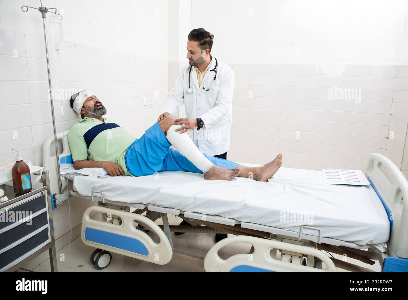 Indian orthopedic doctor examining patient with fractured leg lying on