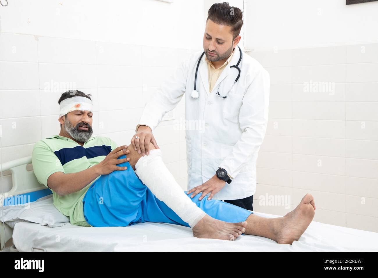 Indian orthopedic doctor examining patient with fractured leg lying on