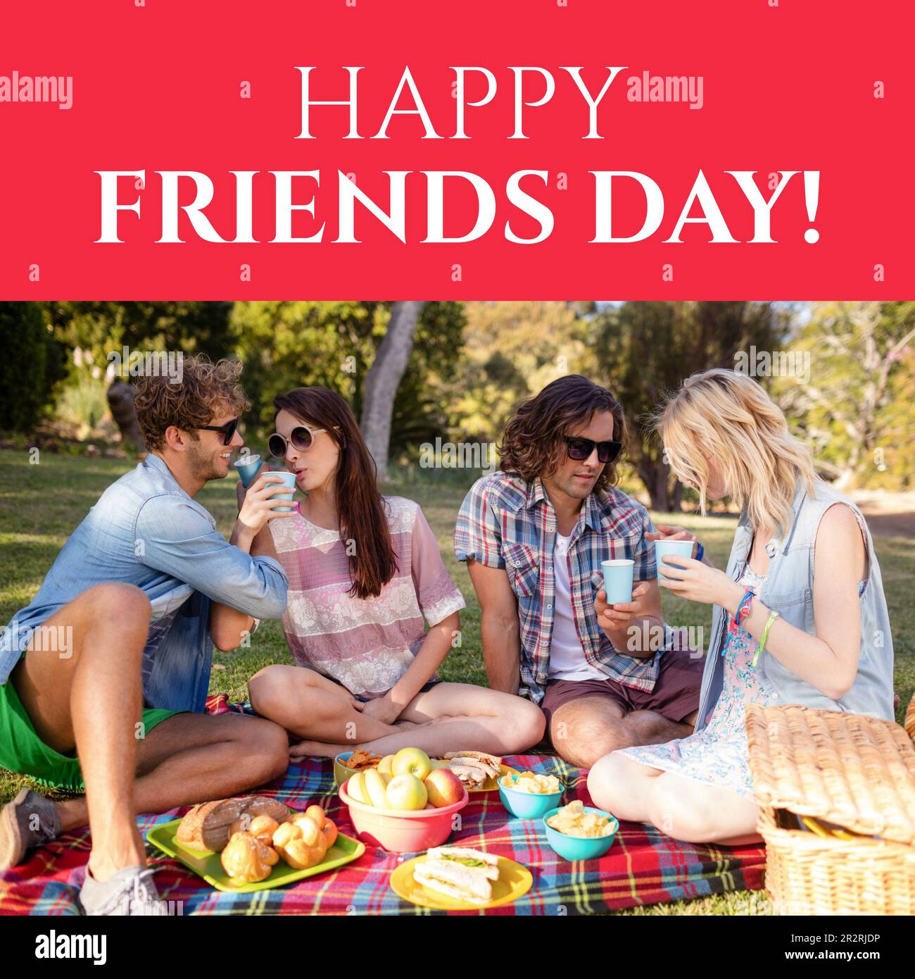 Composition of happy friends day text over happy caucasian friends having picnic in park Stock Photo