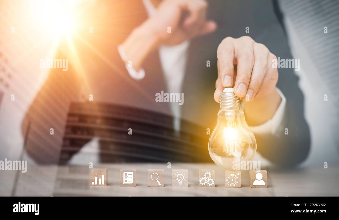 Businessman hand holding light bulb with icon on wood cube and   working on desk, Creativity and innovation are keys to success.Concept of new idea an Stock Photo