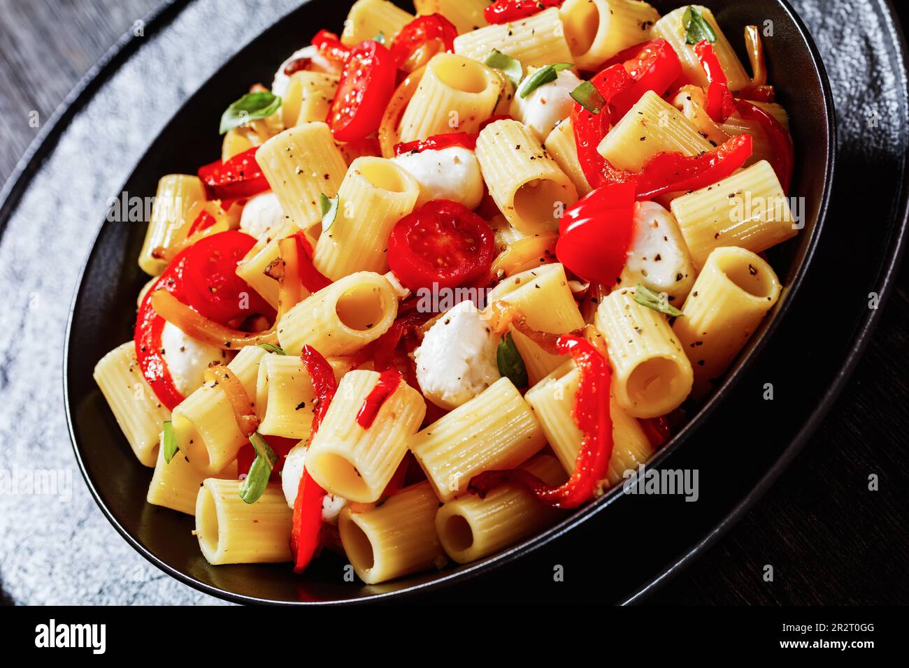 roasted pepper tomato mozzarella pasta salad in black bowl, close-up ...