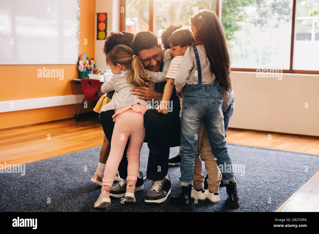 Emotional back to school welcome. Elementary school teacher hugs his students as they return to class. Man greeting his students in a primary school c Stock Photo