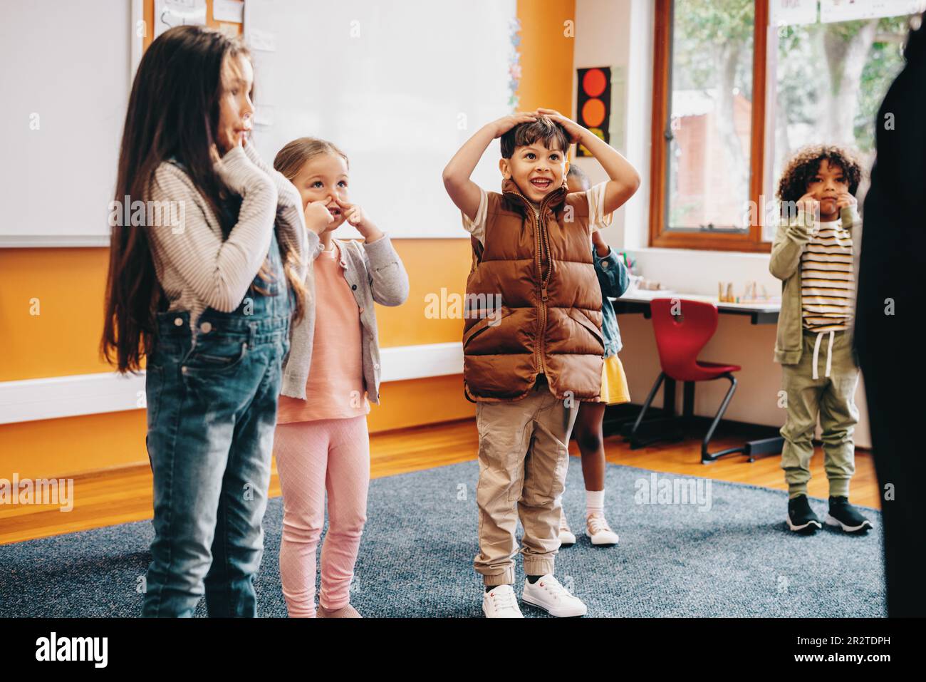 Kids sing and move along to an educational rhyme in class. Group of primary school children participating in a class activity with the instruction of Stock Photo