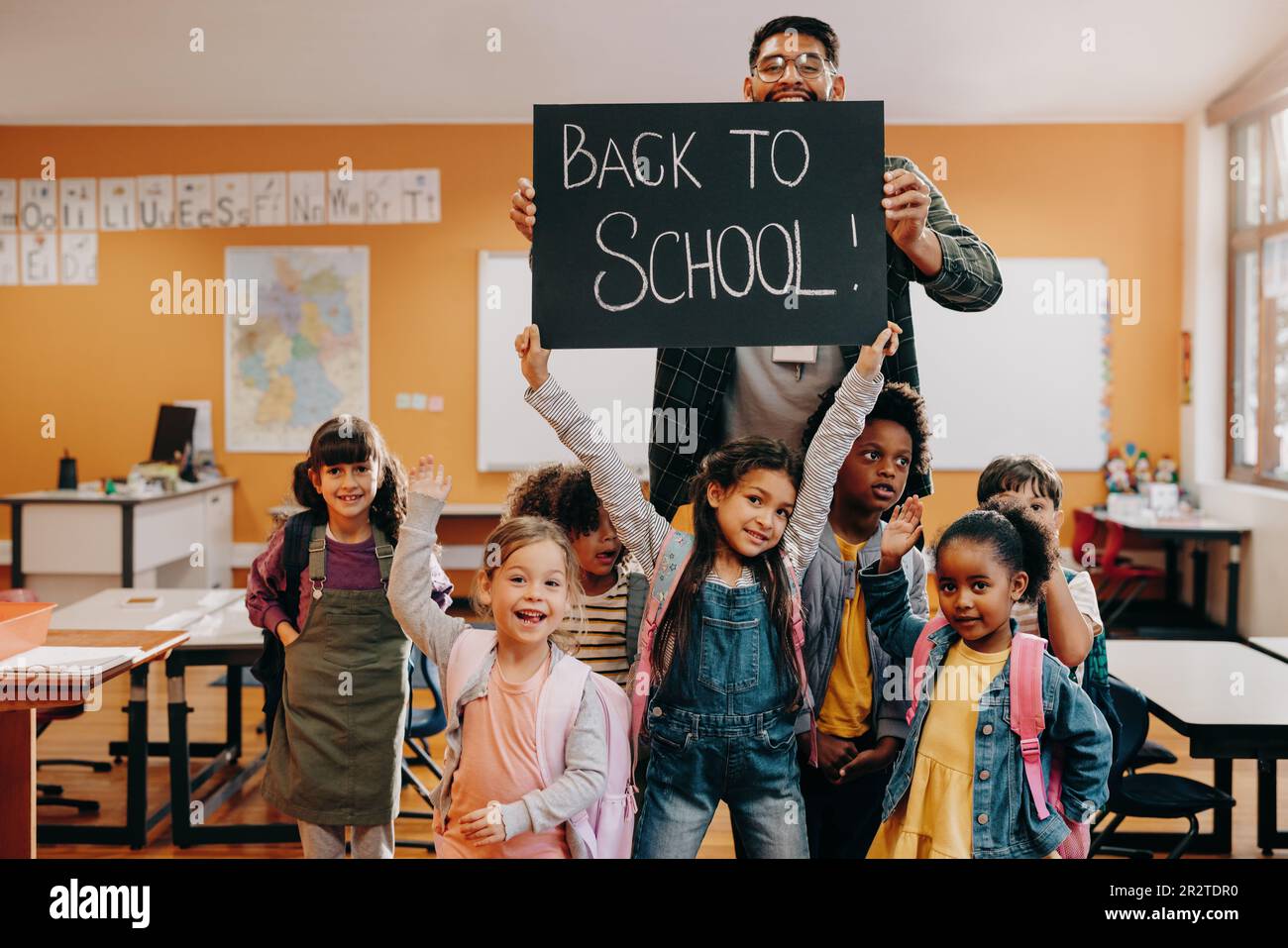 Teacher and students holding up a back to school sign in a classroom. Elementary school class is excited to return to school and enter a new grade. Ba Stock Photo