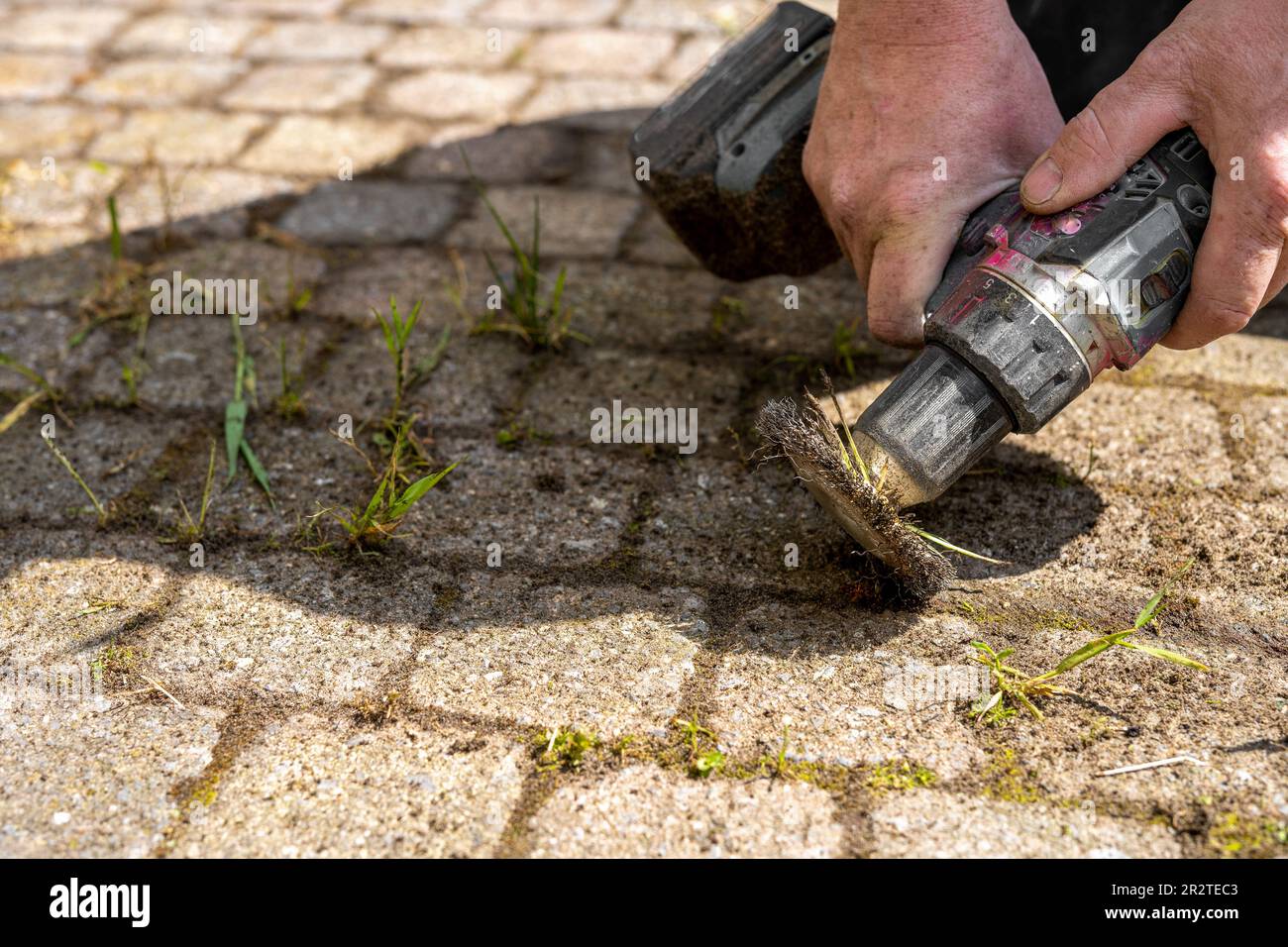 Worker mechanically removing weeds between paving stones in the garden
