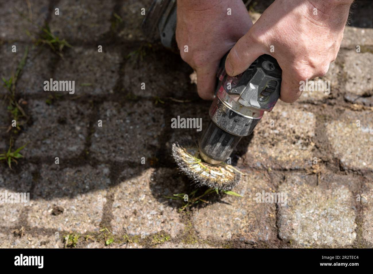 Worker mechanically removing weeds between paving stones in the garden