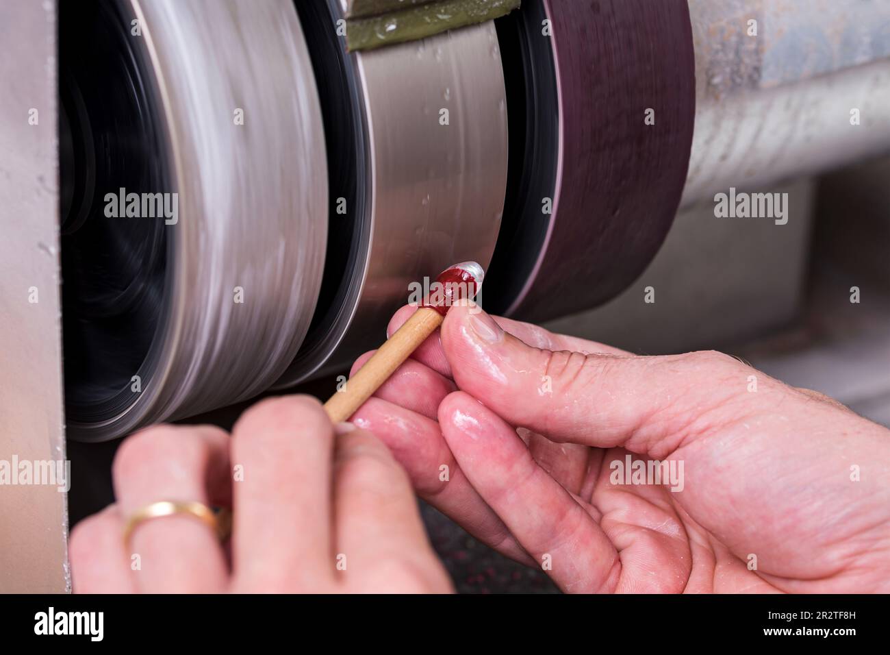 craftsman rolling a wooden stick under a metal lap with the white gemstone on it during cutting process on cabochon machine Stock Photo