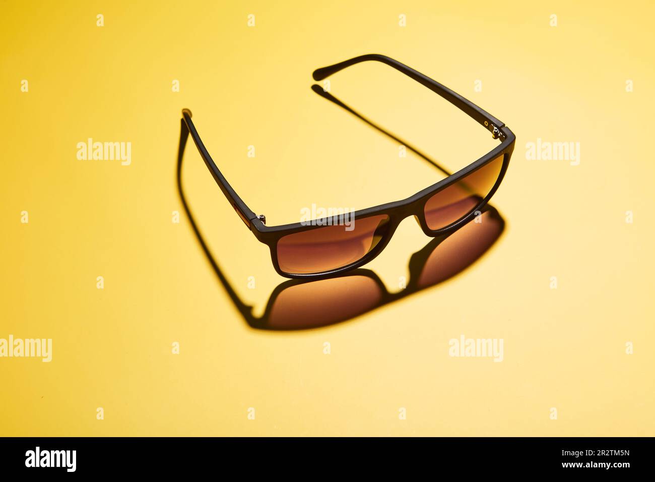 Modern rimmed sun shades, glasses, sunwear casting shadow on yellow