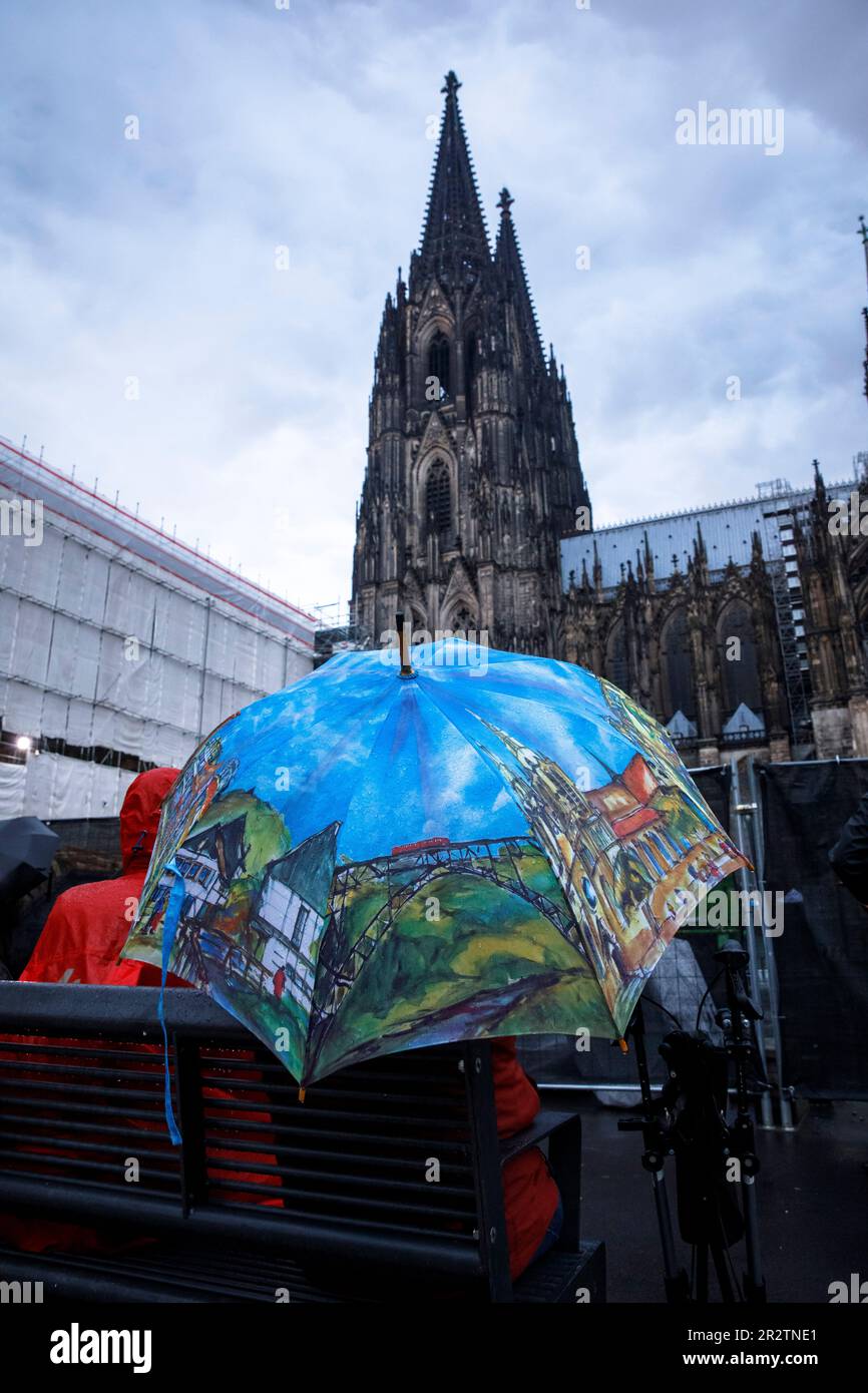 people sitting in the rain at Roncalliplatz in front of the cathedral listening to a bell concert, Cologne, Germany. Menschen sitzen bei Regen auf dem Stock Photo