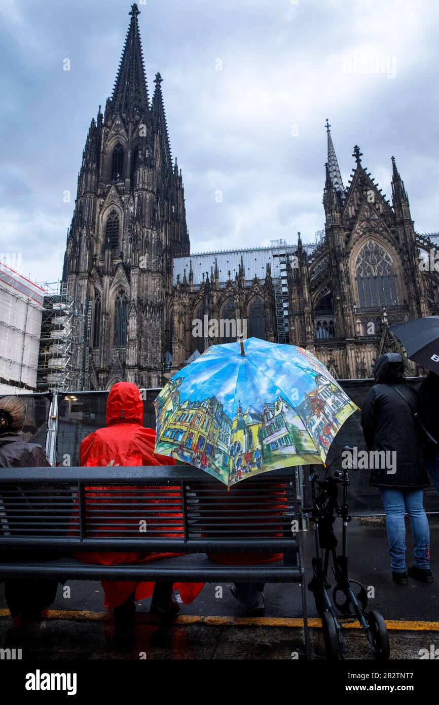 people sitting in the rain at Roncalliplatz in front of the cathedral listening to a bell concert, Cologne, Germany. Menschen sitzen bei Regen auf dem Stock Photo