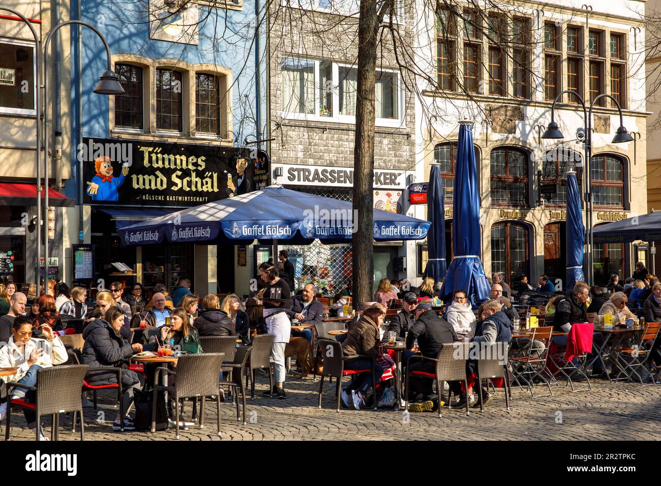 people sitting in front of pubs at the Old Market in the old part of the town, at right the pub Gaffel, Cologne, Germany. Menschen sitzen vor Kneipen Stock Photo