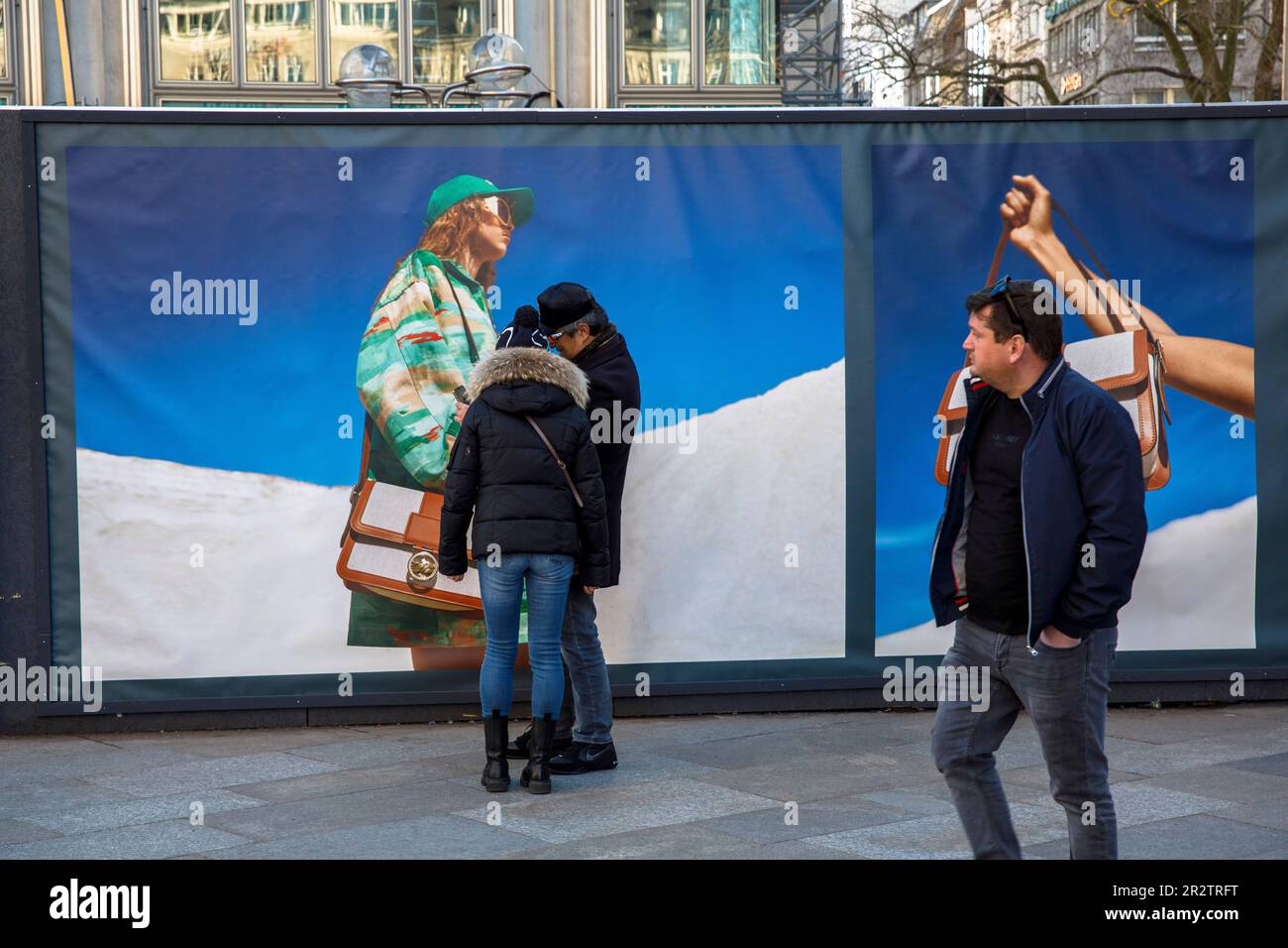 a couple stands in front of a construction fence with advertising posters near the cathedral, Cologne, Germany. ein Paar steht vor einem Bauzaun mit W Stock Photo
