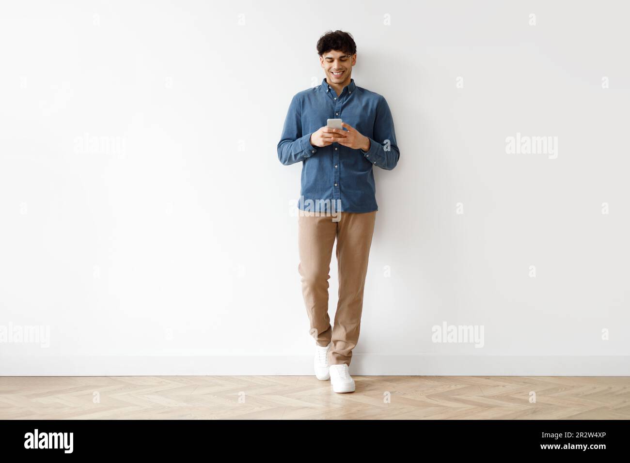 Young Arab Man Using Phone Standing Against White Studio Wall Stock Photo