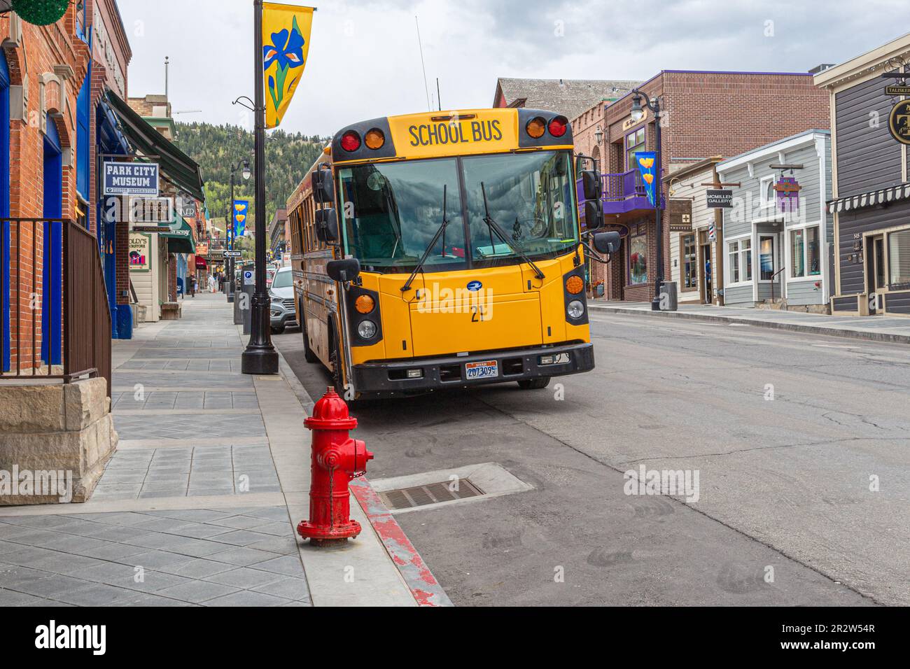 An iconic yellow American school bus parked in front of a red fire hydrant and against the backdrop of Park City in Summit County, Utah, USA Stock Photo