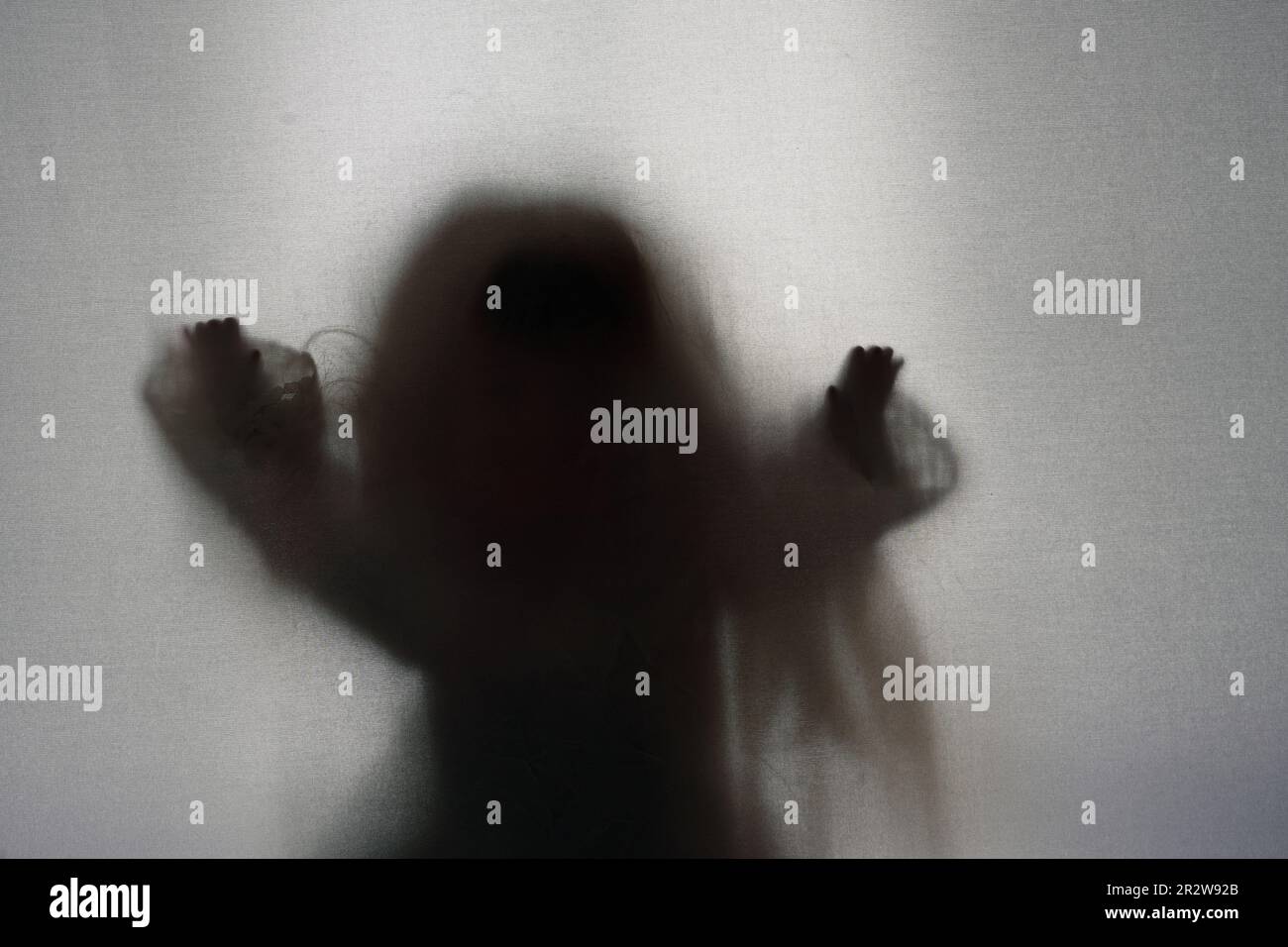 A horror concept of a spooky female doll. Silhouetted and blurred through a sheet. Trying to reach out and break free. Stock Photo