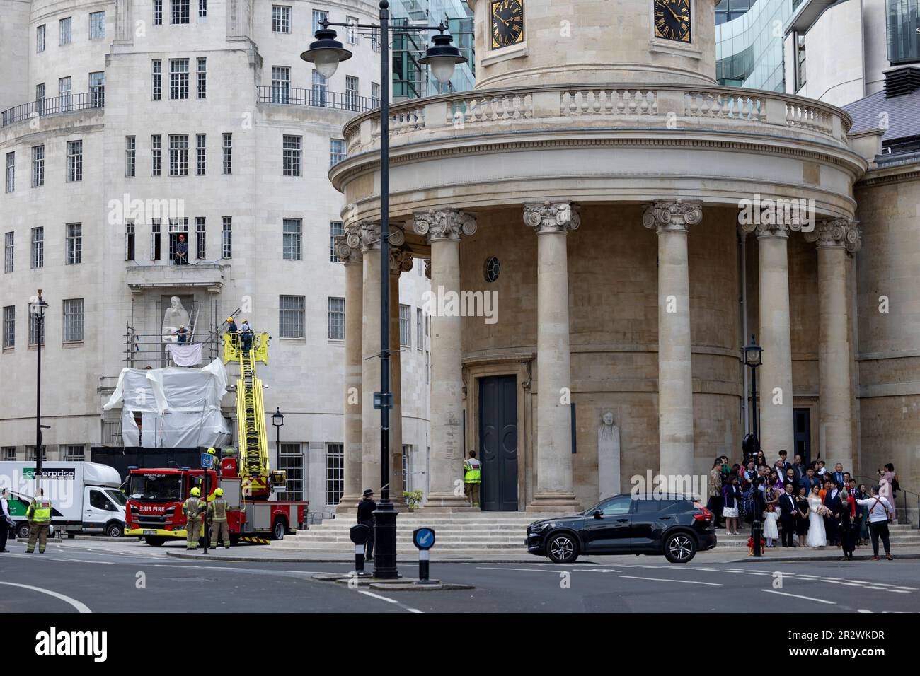 London, UK. 20th May, 2023. A wedding is taking place at the church nearby while the Met Police is dealing with the protester who is hammering the Eric Gill's Prospero and Ariel Statue outside the Broadcasting House. A man climbed scaffolding Broadcasting House and was damaging Eric Gill's Prospero and Ariel Statue since 4am in the morning. Scaffolding was placed recently to be repaired from the damages done during January protest. (Photo by Hesther Ng/SOPA Images/Sipa USA) Credit: Sipa USA/Alamy Live News Stock Photo