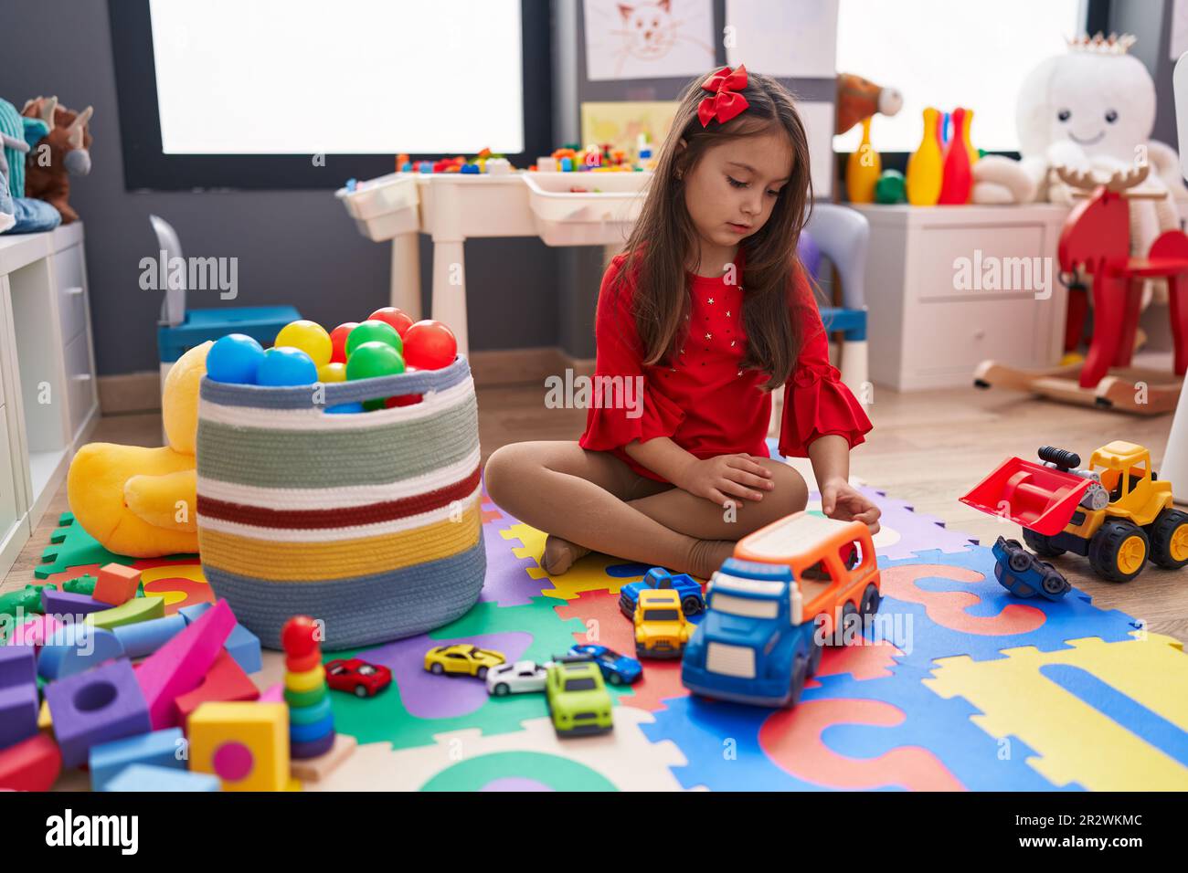 Adorable hispanic girl playing with car toy sitting on floor at ...
