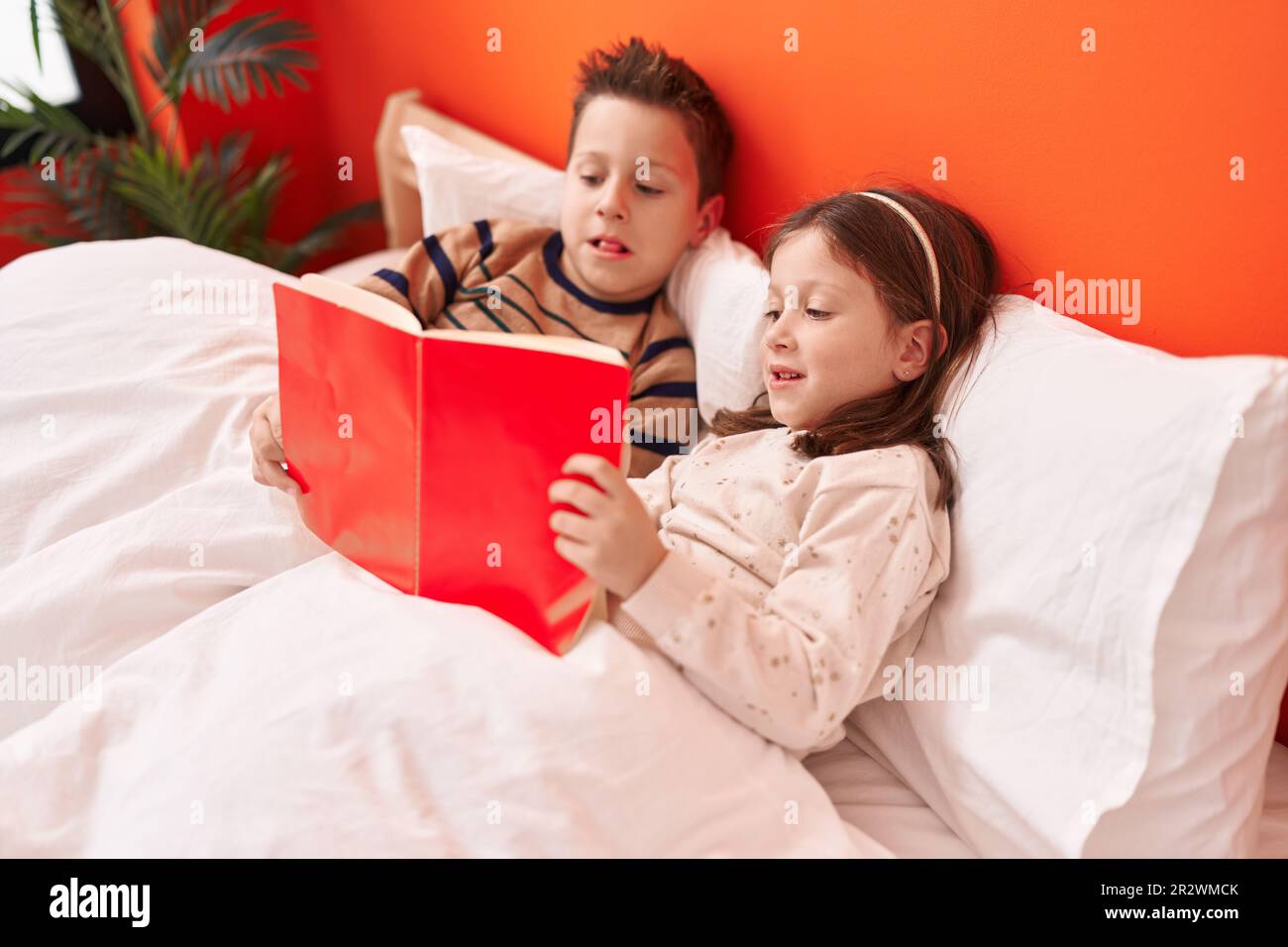 Adorable boy and girl reading book sitting on bed at bedroom Stock ...