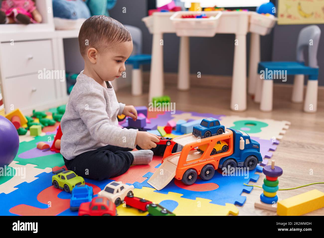 Adorable hispanic boy playing with car toy sitting on floor at ...