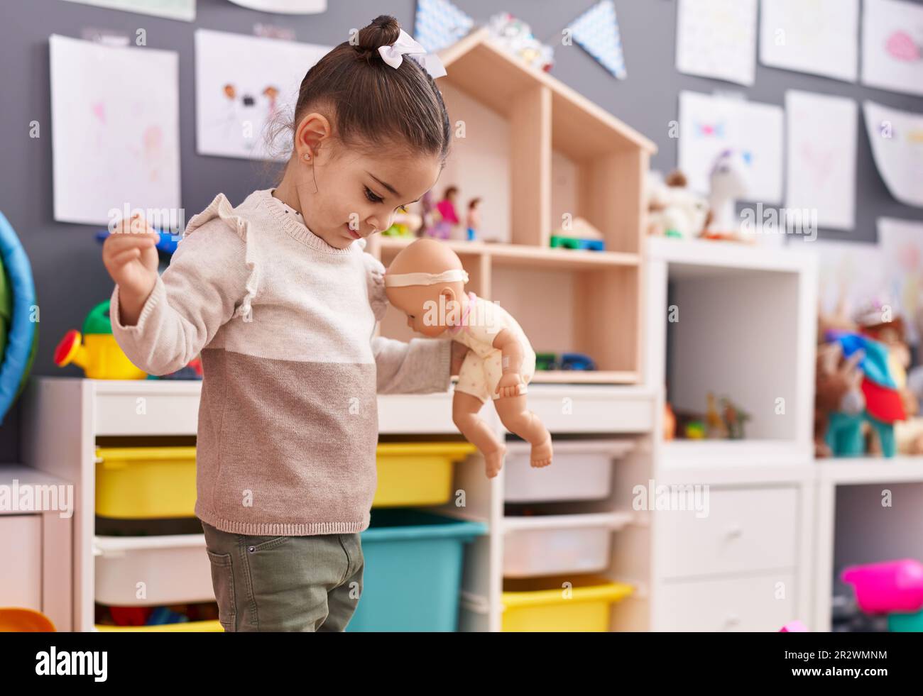 Adorable hispanic girl playing with baby doll standing at kindergarten Stock Photo - Alamy