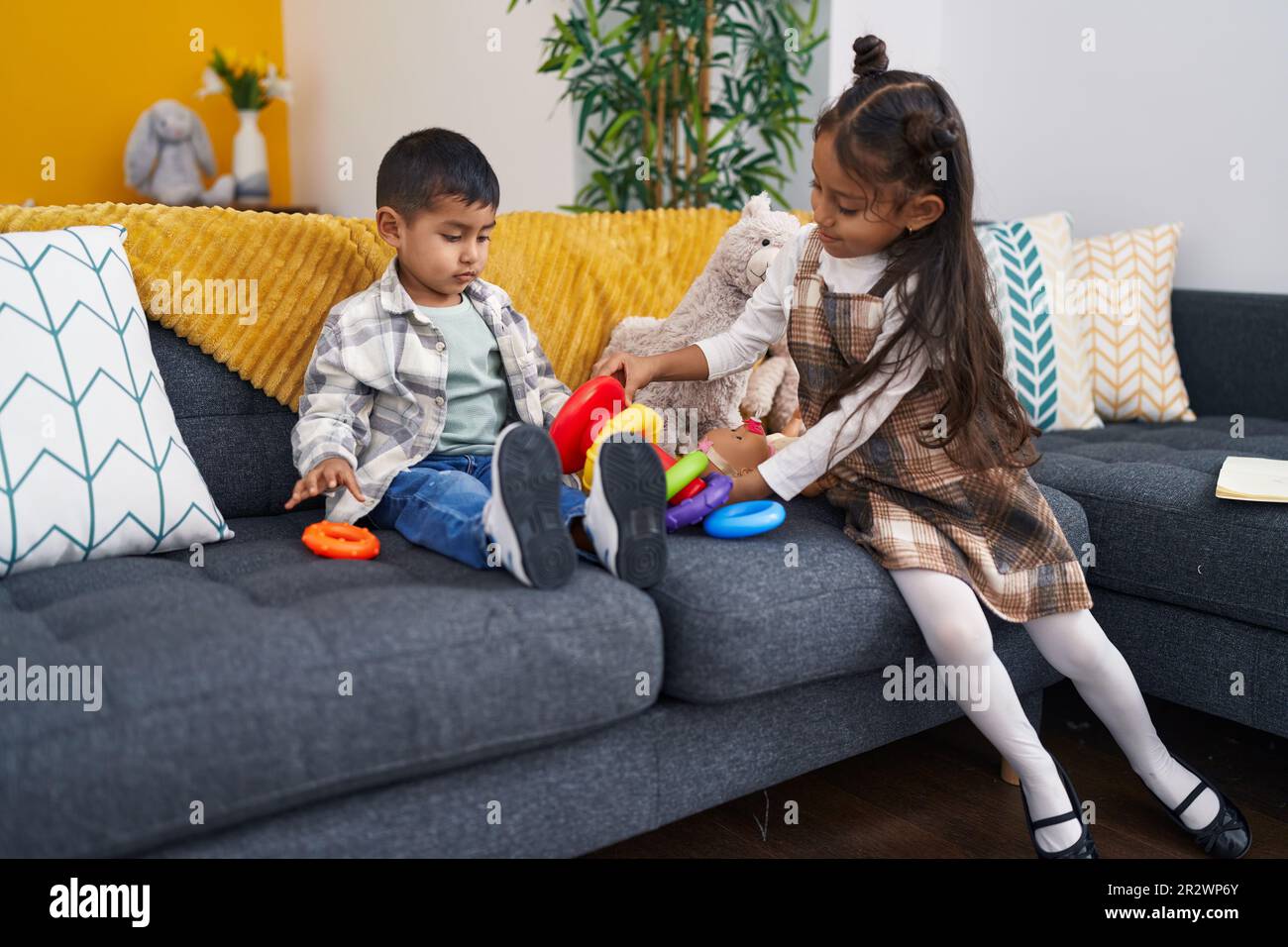 Adorable boy and girl playing with hoops game sitting on sofa at home ...