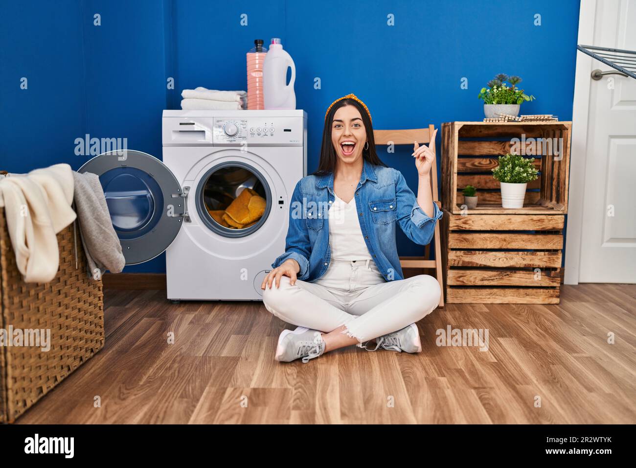 Hispanic woman doing laundry sitting on the floor pointing finger up ...