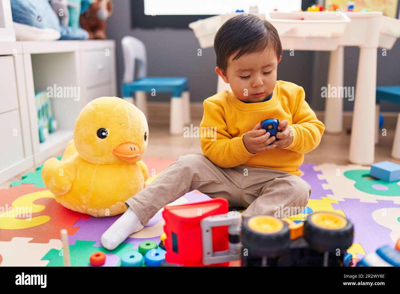 Adorable hispanic boy playing with car toy sitting on floor at ...