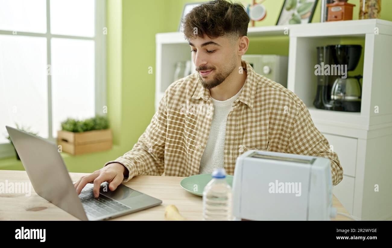 Young arab man having breakfast using laptop at home Stock Photo