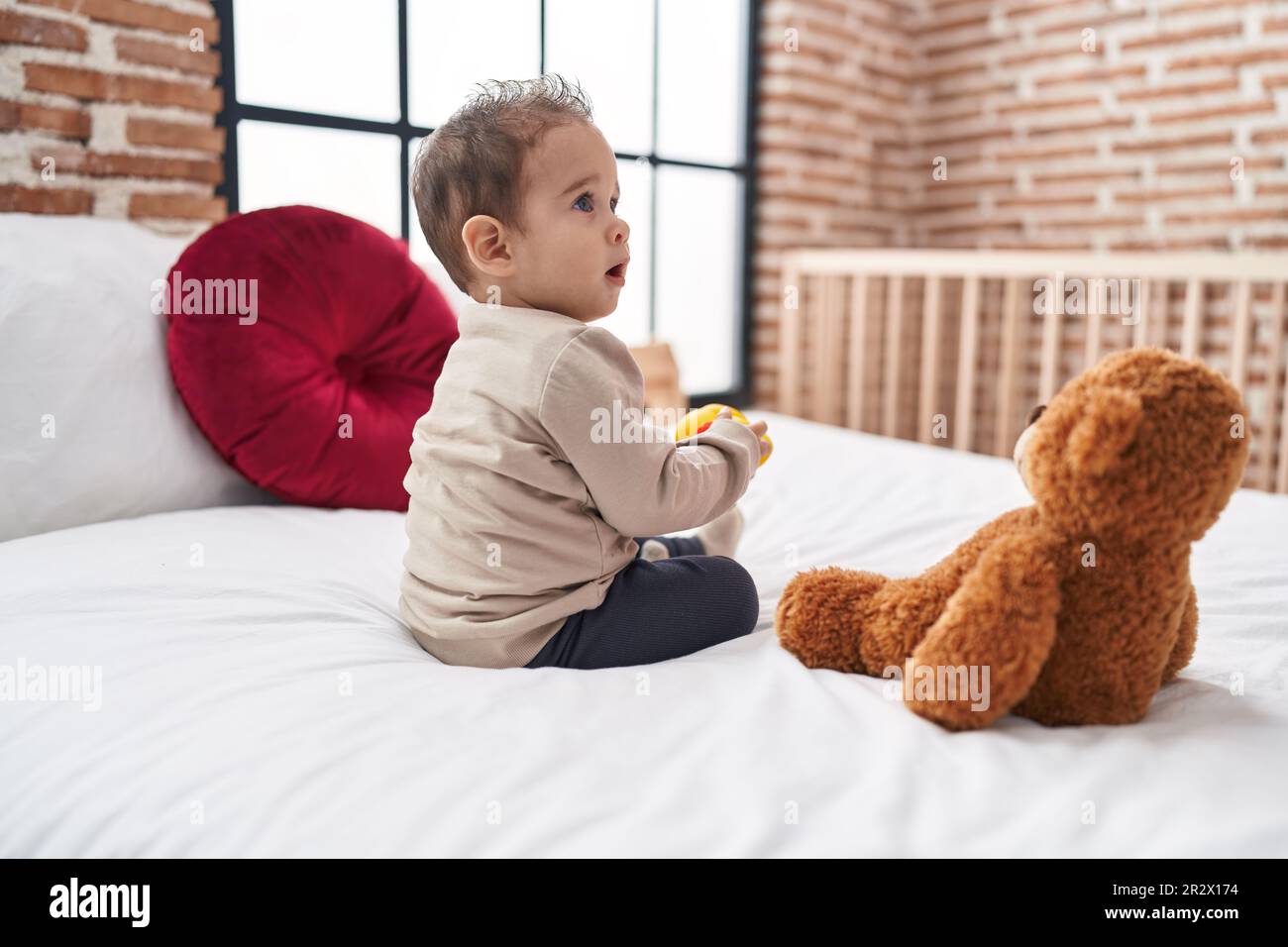 Adorable hispanic boy holding duck toy sitting on bed at bedroom Stock Photo