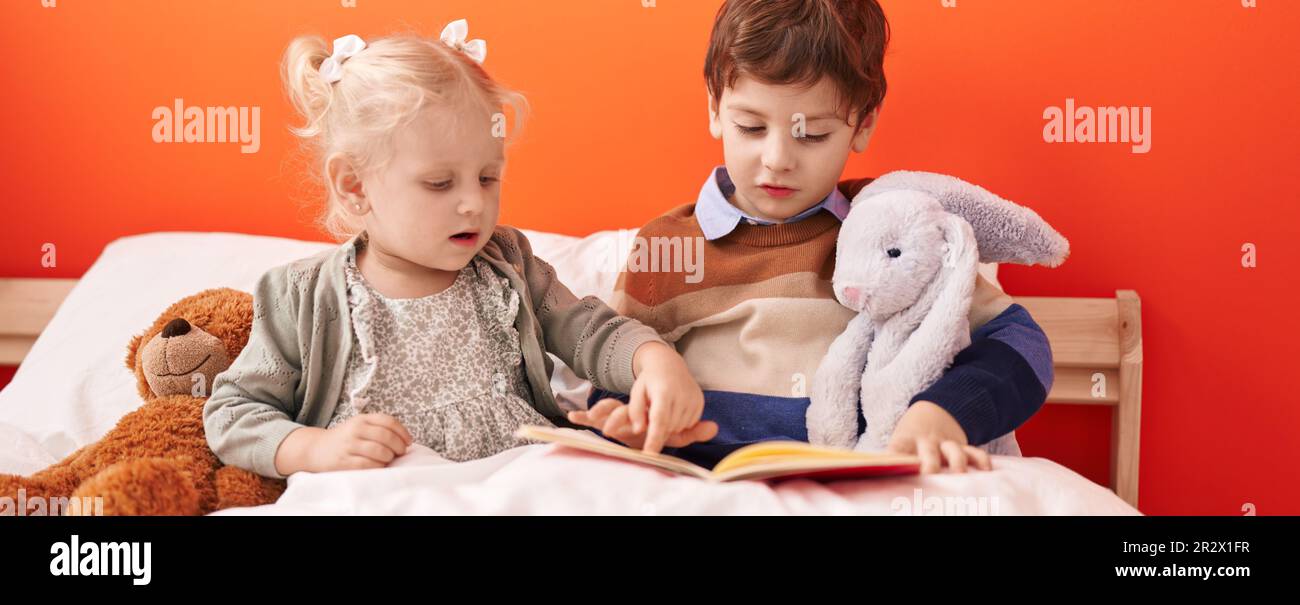 Adorable boy and girl reading book sitting on bed at bedroom Stock ...