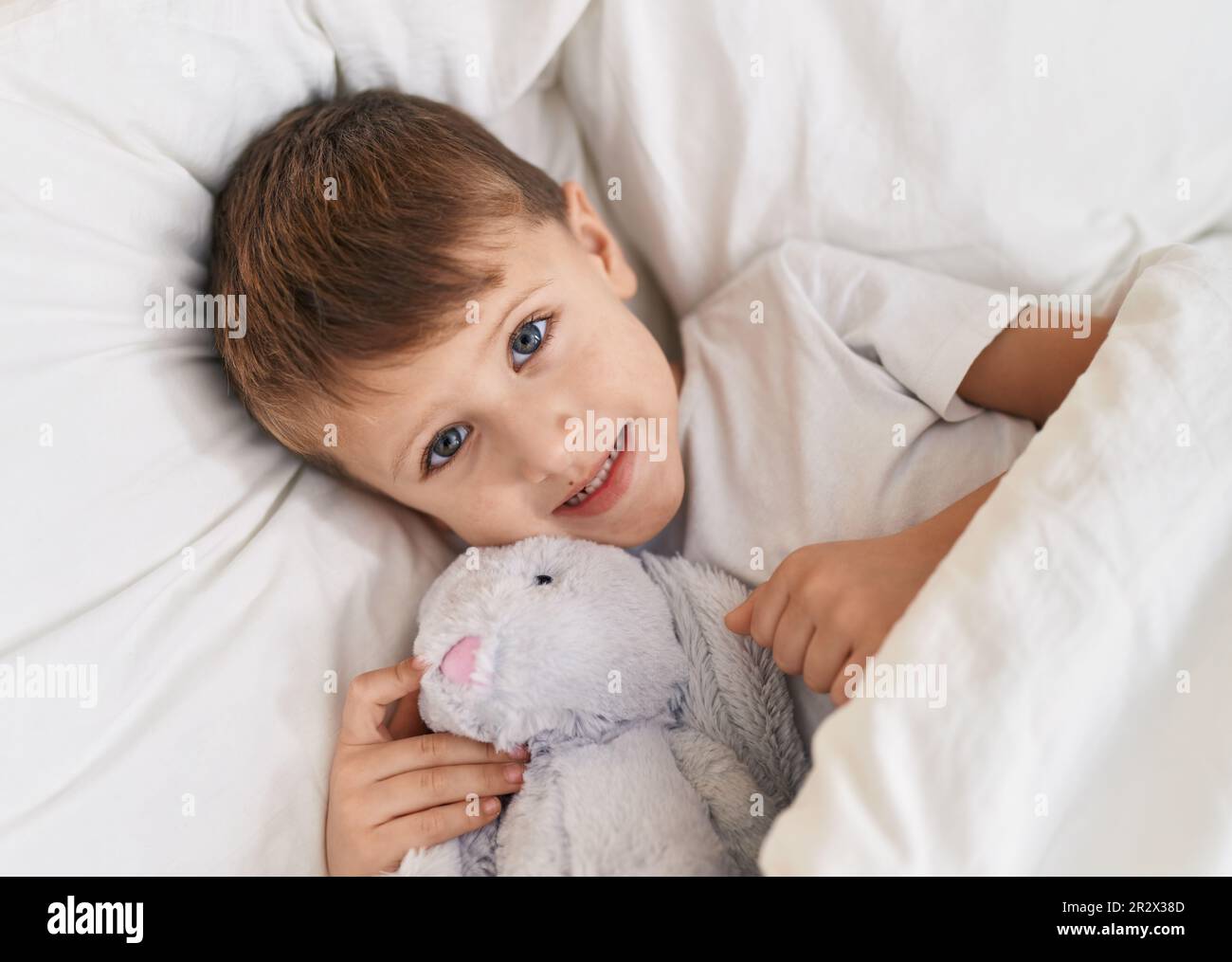 Adorable caucasian boy lying on bed with doll at bedroom Stock Photo ...