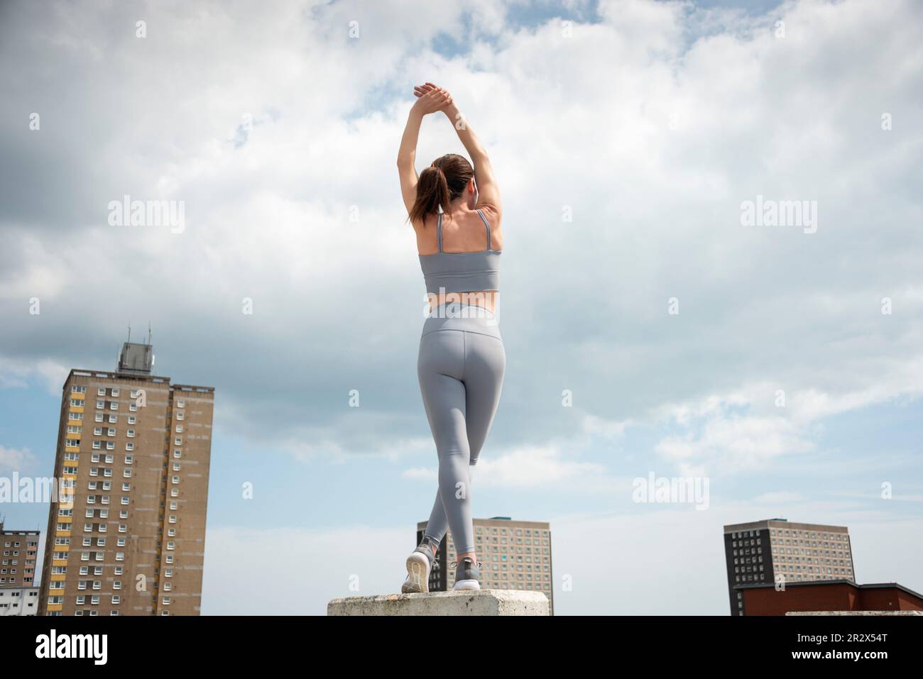 fit, sporty woman doing an arm stretch outside, outdoor exercise, urban setting. Stock Photo