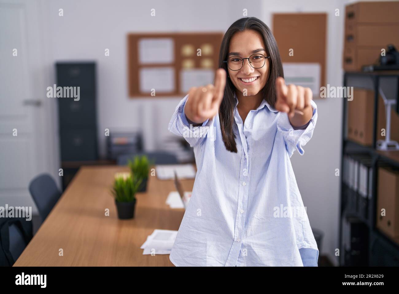 Young hispanic woman at the office pointing to you and the camera with ...