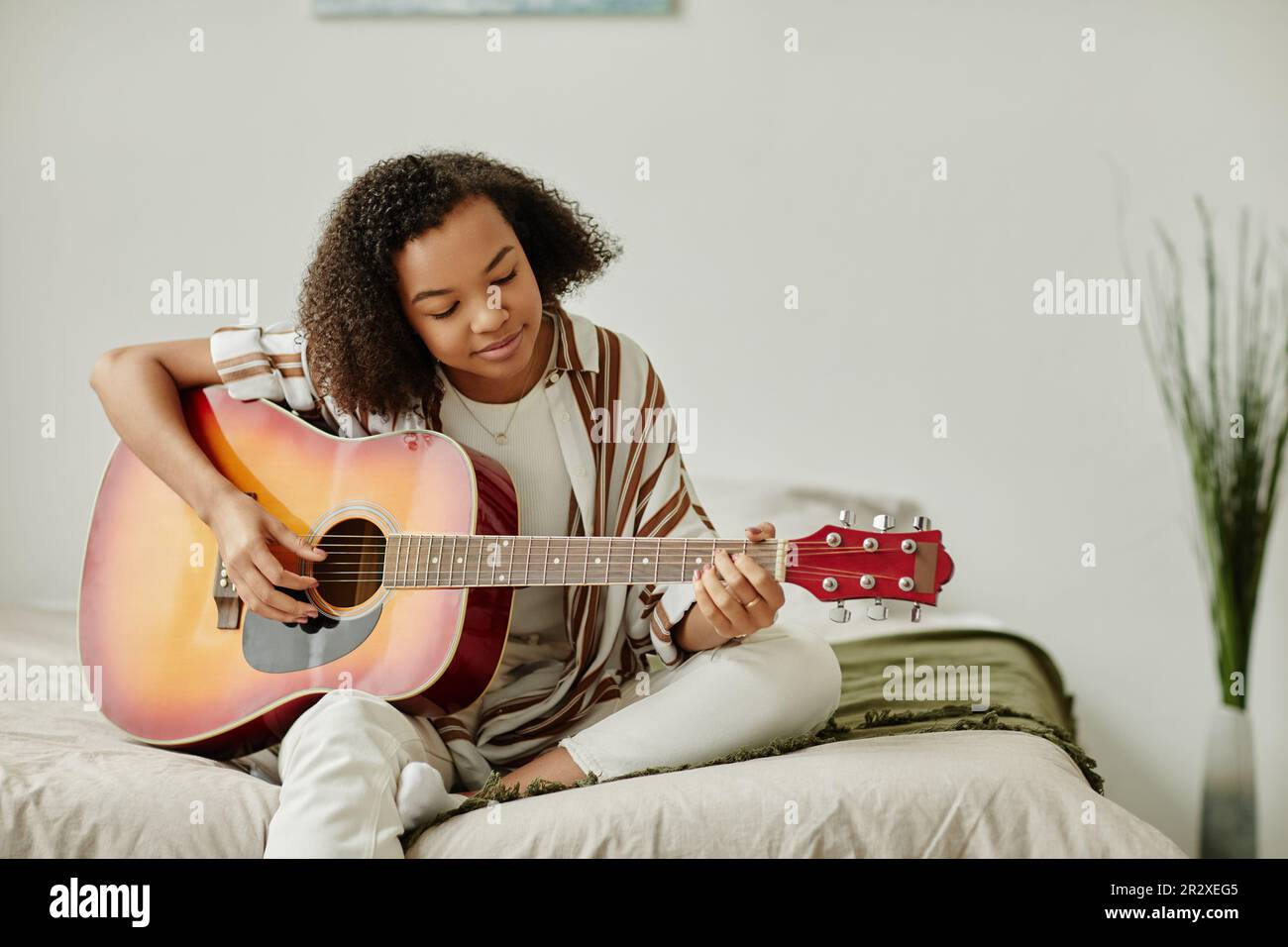 Minimal portrait of black young woman playing acoustic guitar at home ...