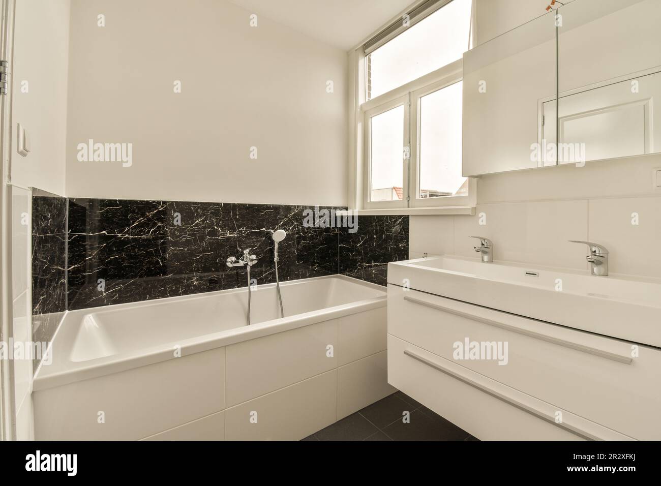 https://c8.alamy.com/comp/2R2XFKJ/a-modern-bathroom-with-black-and-white-marble-tiles-on-the-walls-tub-sink-and-mirror-in-it-2R2XFKJ.jpg