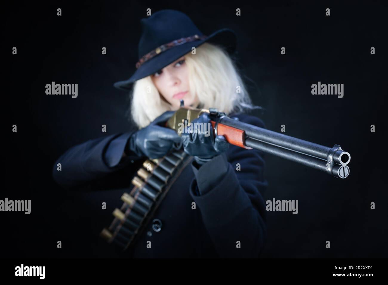 Old west blonde girl in black hat with gun on black background Stock Photo