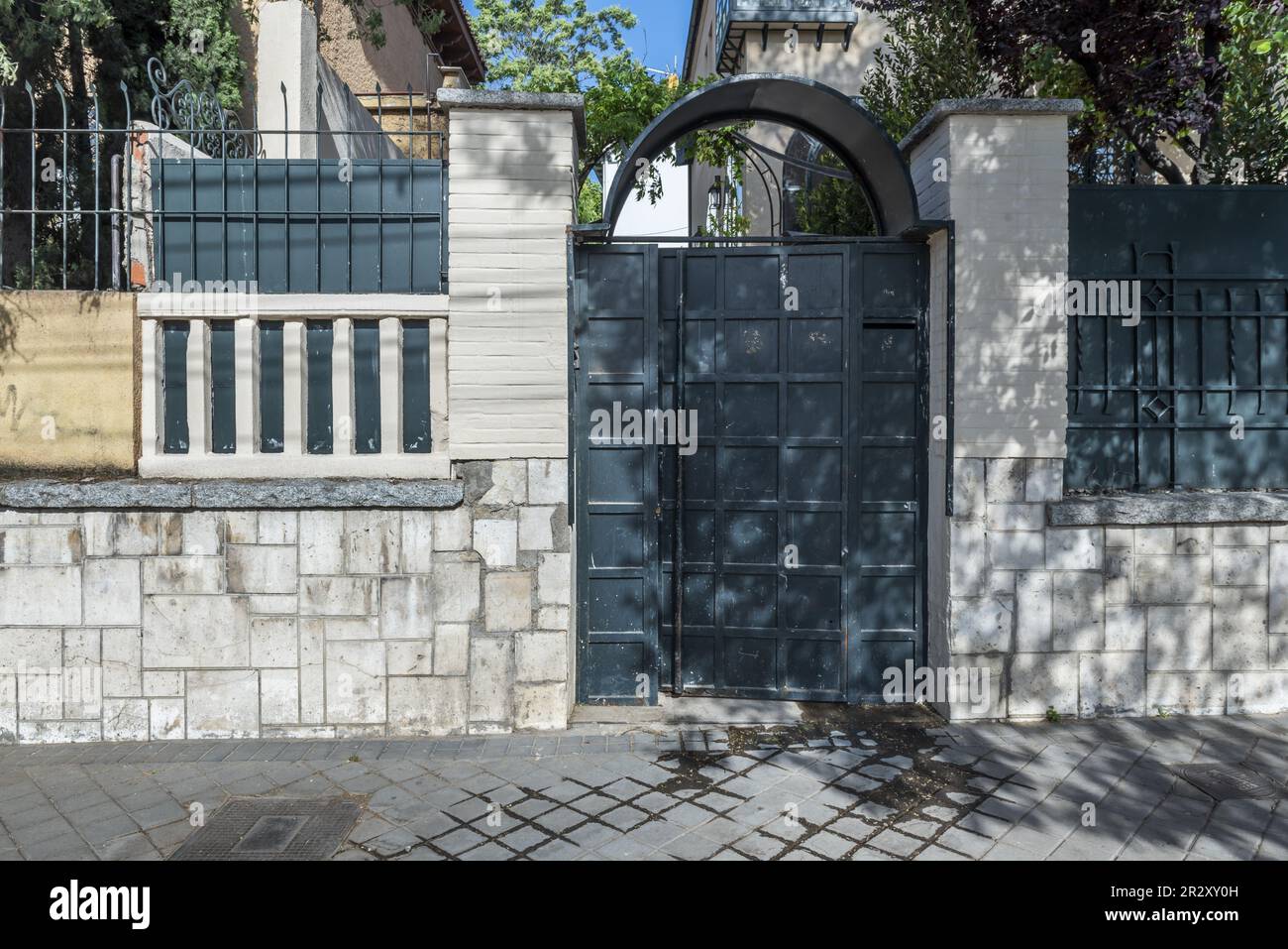 Portal of an urban single-family house with a metal fence painted gray and a wall of irregular stones Stock Photo