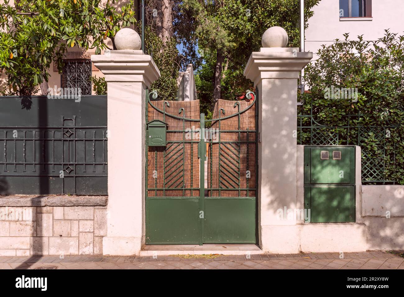 Portal of an urban single-family house with a metal fence with dark green painted wrought iron works combined with stone, hedges and trees Stock Photo