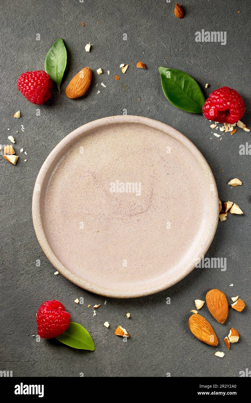 empty pink plate on grey kitchen table with raspberries and almonds for serving ice cream or dessert, top view Stock Photo