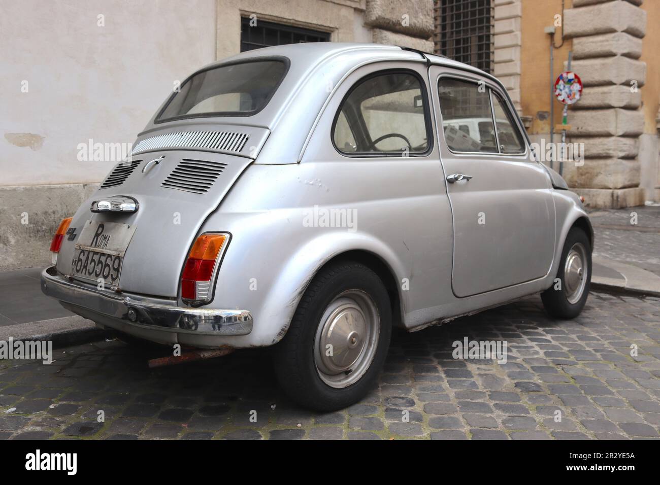 Fiat 500 in battle scarred condition evident to driving the streets of Rome for years. Despite bubbling paint and visible dents, it remains a survivor. Stock Photo