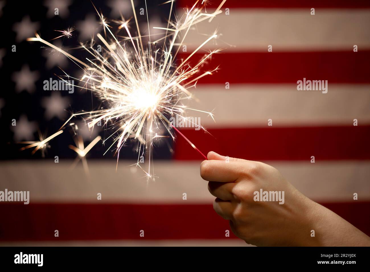Hand holding lit sparkler in front of the American Flag for 4th of July ...