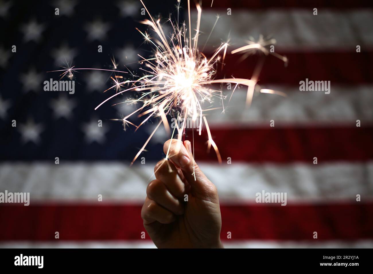 Hand holding lit sparkler in front of the American Flag for 4th of July ...