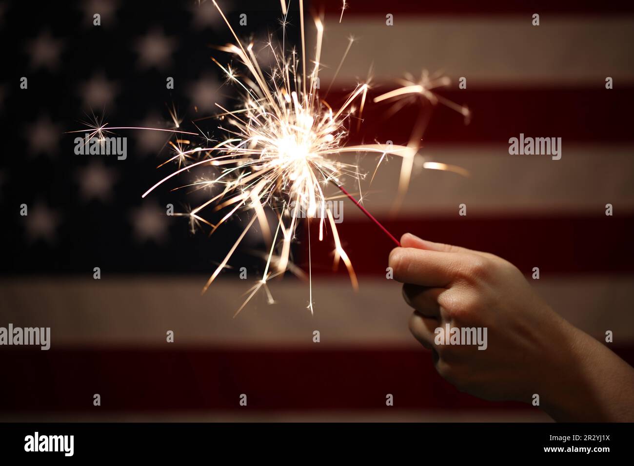 Hand holding lit sparkler in front of the American Flag for 4th of July ...